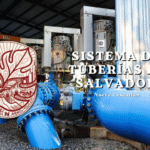 Daños en tuberías en Nuevo Cuscatlán: por qué encontrar la causa exige algo más que mirar la obra más cercana Gráfico de la campaña Ciudad Sostenible mostrando la infraestructura industrial del sistema de tuberías y abastecimiento de agua en Nuevo Cuscatlán, El Salvador, destacando grandes motores y conductos azules.